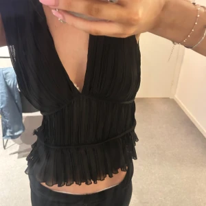 Svart ärmlös blus med volangdetaljer - Snygg svart blus med djup v-ringning och volangdetaljer. Använder inte längre och har en defekt på sidan men inget som syns enligt mig, storlek s💞