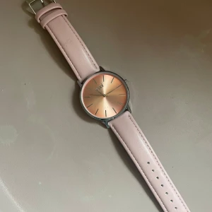 Rosa klocka från Regal - Elegant klocka från Regal med en stilren rosa urtavla och matchande rosa armband. Klockan har en minimalistisk design med silverdetaljer och en bekväm passform. Perfekt accessoar för att lyfta din stil.