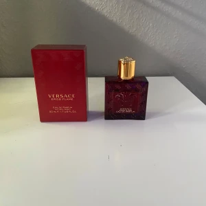 Versace Eros Flame Eau de Parfum - Versace Eros Flame Eau de Parfum i en elegant röd flaska med guldlock. Doften är intensiv och maskulin, perfekt för den självsäkra mannen. Flaskan har en stilren design med Versace-logotypen ingraverad.