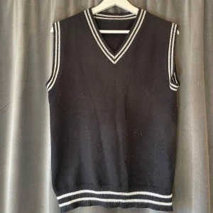 Svart väst - Snygg svart stickad väst med vita ränder vid ärmslut, hals och nederkant. Den har en klassisk v-ringad design som ger en stilren look. Perfekt för att lägga till en extra touch till din outfit.⭐️