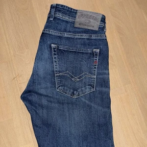 Blå jeans från Replay - Snygga blå jeans från Replay med klassisk femficksdesign och en diskret logga på bakfickan. Jeansen har en knappgylf och är tillverkade i ett slitstarkt denimtyg. Perfekta för en avslappnad stil.