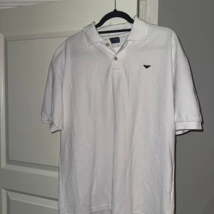 Vit kortärmad pikétröja från Armani - Säljer en stilren vit pikétröja från Armani Jeans. Tröjan har korta ärmar och en klassisk krage med knappar. Perfekt för en avslappnad men ändå elegant look.