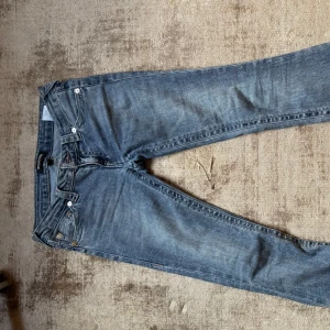 Blå jeans från True Religion - Snygga blå jeans från True Religion! Byxorna har rosa sömmar och har lite defekt längst ner vid fötterna! 
