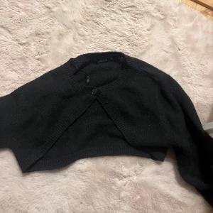 Svart bolerotopp från Gina Tricot - Säljer en stilren svart bolerotopp från Gina Tricot. Den har en enkel knapp framtill och är perfekt för att lägga till en extra touch till din outfit. Passar bra över klänningar eller toppar.