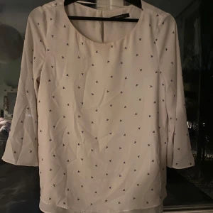 Ljusrosa blus med små mönster - Säljer en stilren vit blus med små diskreta mönster. Blusen har trekvartsärmar och en rund halsringning. Perfekt för en elegant och avslappnad look.