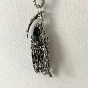 Silverfärgat halsband med lieman-hänge - Unikt halsband med ett detaljerat hänge föreställande en lieman. Hänget är i silverfärg och har en dramatisk design med en skarp lie. Perfekt för att ge en edgy touch till din stil.