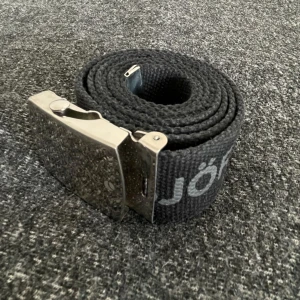 Svart bälte från Björn Borg - Snyggt svart bälte från Björn Borg med silverfärgat spänne. Perfekt för att ge din outfit en sportig touch. Bältet har märkets logga tryckt längs bandet och ett stilrent metallspänne.
