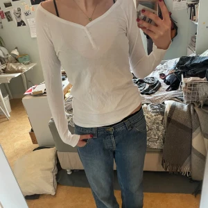 Vit långärmad topp från Ellos - Säljer en stilren vit långärmad topp från Ellos i ekologiskt material. Toppen har en v-ringad design med knappar framtill. Perfekt för en avslappnad look. Passar bra till jeans eller kjol.