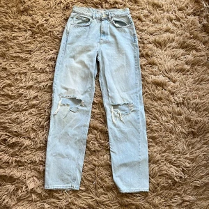 Ljusa jeans med slitningar - Säljer ett par ljusa jeans med slitningar på knäna. Det finns en svag gul fläck vid gylfen annars är den i fint skick.