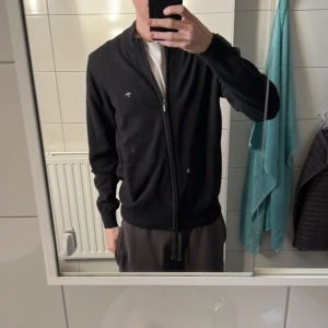 Svart halvzip från Fynch-Hatton - Säljer en stilren svart kofta från Fynch-Hatton i superfint 3-lagers bomull. Koftan har dragkedja framtill och en liten broderad logga på bröstet. Perfekt för en avslappnad och snygg look. Nypris 1199 kr