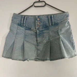 Ljusblå jeanskjol - Trendig ljusblå jeanskjol med knappar framtill och veckade detaljer. Perfekt för en avslappnad stil. Kjolen har en kort längd och en klassisk jeanslook.