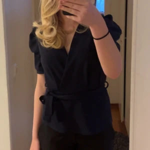Marinblå omlottblus med knytband - Snygg svart omlottblus med korta puffärmar och knytband i midjan. Jättefin pris kan diskuteras❤️
