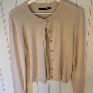 Beige kofta från 157 - Säljer en stilren beige kofta från 157 i storlek M. Koftan har långa ärmar och knäpps med matchande knappar framtill. Perfekt för en enkel och klassisk look.