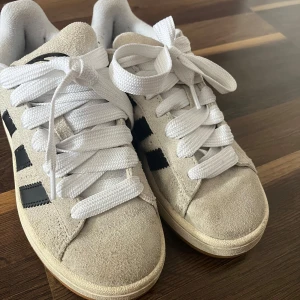 Adidas Campus sneakers beige mocka - Säljer ett par Adidas Campus sneakers i beige mocka med svarta ränder och vit sula. Skorna har klassisk rund tå, platt gummisula och kommer med både vita och svarta skosnören. Storlek 36 2/3