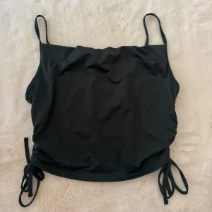 Svart topp med snörning SHEIN - Svart topp från SHEIN i storlek XL. Modellen har smala axelband och snygga snörningsdetaljer i sidorna som kan justeras för perfekt passform. Materialet är stretchigt och snabbtorkande