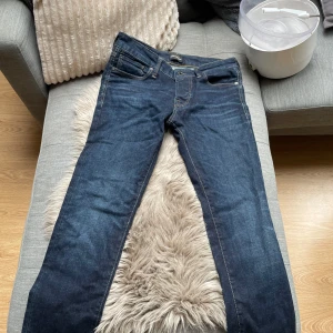 Jack & Jones Slim Glenn jeans blå 29/30 - Mörkblå jeans från Jack & Jones, modell Slim Glenn. Snygg slim fit med klassisk femficksdesign och kontrastsömmar. Tillverkade i bomull med lite stretch för skön passform. Perfekta för dig som gillar en smal siluett och stilrena detaljer.