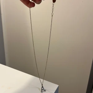 Halsband med bokstav A i silver - Snyggt halsband med en tunn kedja i guldton och ett hängsmycke i form av bokstaven A i silverfärg. Perfekt accessoar för dig som vill ha något personligt och stilrent runt halsen.