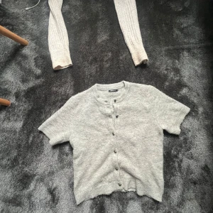 Kortärmad stickad  - Superfin ljusgrå kofta från Gina Tricot med korta ärmar och rund hals. Koftan är stickad i mjukt material och har knappar hela vägen framtill. Perfekt att slänga över en topp för en chill look.    SKRIV FÖR FLER BILDER 