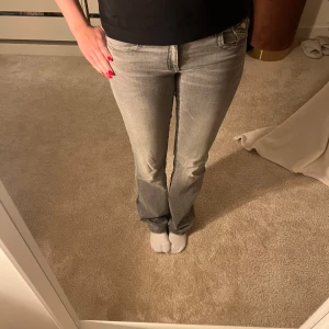 Grå bootcut jeans med fickdetaljer - Säljer ett par grå Low waist jeans med bootcut-modell och snygga fickdetaljer bak från Gina Tricot Young. 