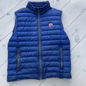 Blå dunväst från Colmar - Snygg blå dunväst från Colmar med quiltad design och hög krage. Västen har två dragkedjeförsedda fickor och en tydlig Colmar-logga på bröstet. Insidan är ljusgrå och materialet är lätt och smidigt, perfekt nu till hösten det är väldigt bra skick på den 9/10 