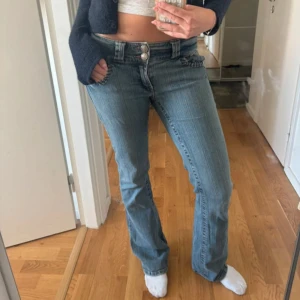 Blå bootcut jeans med låg midja - Snygga blå bootcut jeans med låg midja och coola detaljer på fickorna, dekorativa sömmar och dubbla knappar framtill. Från a2vintage. innebenslängd 82cm och midjemått 37cm (rakt över).