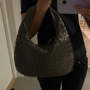 Flätad brun axelväska  - Säljer en snygg brun väska med flätad design. Väskan har en rundad form och är tillverkad i mjukt skinn. Perfekt storlek för att få plats med allt du behöver och har ett stilrent uttryck som lyfter vilken outfit som helst. Använd fåtal gånger