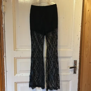 Svarta spetsbyxor från SHEIN XS - Svarta byxor från SHEIN i storlek XS med utsvängda ben och transparent spetsmaterial. Byxorna har hög midja med inbyggda shorts, medan benen är helt i spets. 