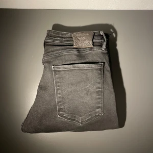 Jack and Jones jeans svarta - Svarta slim fit jeans från Jack & Jones, modell slim Glenn. Klassisk femficksdesign med snyggt läderpatch bak i midjan. Jeansen har en smal passform och är tillverkade i stretchigt material för extra komfort.