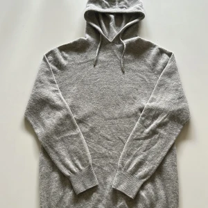 Grå Kashmir/merinoull hoodie - Mysig grå hoodie i merinoull med huva. Tröjan har långa ärmar och ribbade muddar vid ärmslut och nederkant. Perfekt för dig som gillar en enkel och stilren look.