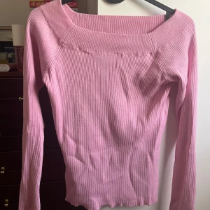 Rosa ribbad långärmad tröja - Säljer en ljusrosa långärmad tröja med ribbad struktur och bred, off shoulder halsringning. Tröjan är figurnära och har stretchigt material som sitter snyggt på kroppen. Perfekt för dig som gillar en enkel men ändå söt stil.