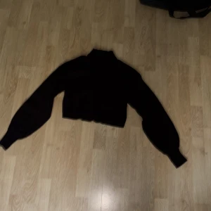 Svart croppad polotröja Gina Tricot - Svart croppad polotröja från Gina Tricot med långa ärmar och ribbade muddar. Tröjan är stickad och har en hög hals, perfekt för att skapa en snygg och trendig look till hösten och vintern.