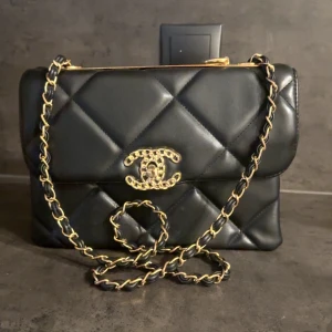 Svart quiltad handväska i skinn - Säljer en ikonisk svart quiltad handväska f i mjukt skinn med guldfärgade detaljer och kedjerem. Klassisk CC-logga framtill och elegant skrift upptill. Perfekt storlek för det viktigaste och en riktig statement piece. Det korta bandet har gått av upptill som man kan se på bilden, men lyckas man skruva bort metallen på andra sidan och putsar den så är den superfin att ha som axelbandsväska också, pris går att diskutera. 