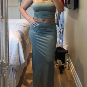 Grön set från Bershka - Snygg långkjol från Bershka i en mjuk, stretchig grön polyester med matchande topp. Kjolen har en tight passform och mellan hög midja som framhäver siluetten. Perfekt för dig som gillar minimalistisk stil och vill ha en enkel men trendig look. Toppen har sömnen gått upp i men annars är setet väldigt fint