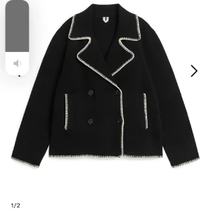 Svart skepparkavaj med kontrastsömmar - Säljer en svart skepparkavaj med vita kontrastsömmar längs krage, fickor och ärmslut. Jackan har dubbelknäppning, bred krage och raka fickor framtill. Perfekt för dig som vill ha en stilren men ändå unik look.FÅR BJUDA