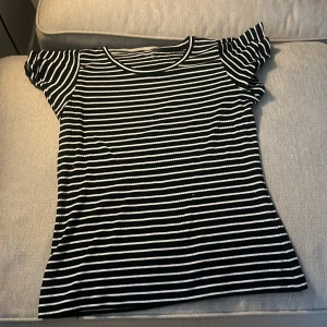 Randig svartvit ribbad topp - Svart och vit randig topp med ribbad struktur och korta volangärmar. T-shirten har rund halsringning och är figurnära i modellen. Perfekt för dig som gillar en enkel men ändå trendig look. Toppen är ifrån Lindex men jag har klippt av lappen! Toppen är storlek 170💕