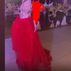 Röd långklänning med glittrig topp - Säljer en röd långklänning med voluminös tyllkjol och glittrig, pärlbeströdd överdel. Klänningen har djup v-ringning och är ärmlös, perfekt för bal eller fest. Toppen är täckt av paljetter och pärlor som ger en riktigt lyxig känsla. Jag har använt tre gånger och det finns några ställe där pärlorna har gått bort men det är inte så synligt. Jag har storlek 34 men den passar även storlek 36. 