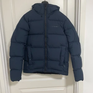 Mörkblå dunjacka Peak Performance M - Säljer en mörkblå dunjacka från Peak Performance i storlek M. Jackan har huva, dragkedja framtill och två stora fickor. Den är quiltad och har en clean, sportig look som passar perfekt när det är kallt ute.