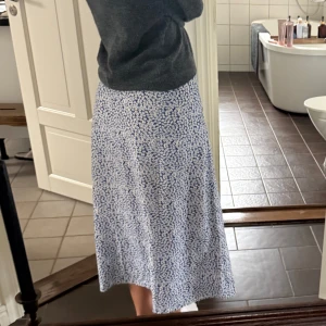 Blommig blå långkjol - Säljer en flowy långkjol med blå botten och små vita blommor över hela tyget. Kjolen har en rak och avslappnad passform som ger en chill vibe. Perfekt för dig som gillar blommigt och vill ha något som sticker ut lite extra under vår och sommar.