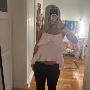 Ljusrosa volangtop med smala axelband - Supersöt ljusrosa topp med volanger både upptill och nedtill. Modellen är croppad och har smala axelband som ger en fräsch och somrig vibe. Perfekt för dig som gillar romantiska detaljer och vill sticka ut med en feminin look.