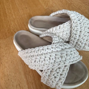 Beige stickade sandaler Inuikii - Snygga sandaler från Inuikii i beige med breda, stickade band i bomull som korsar över foten. Platt sula och öppen tå.