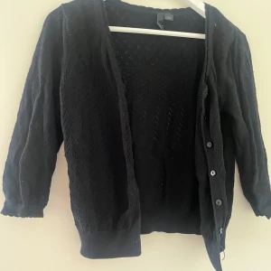 Svart/mörkblå stickad kofta med knappar - Svart/mörkblå stickad kofta från H&M med fina hålmönster och knappar framtill. Koftan är trekvartsärmad. 