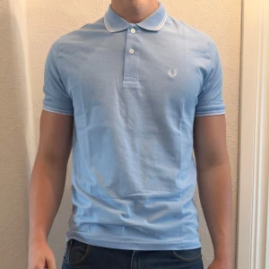 Ljusblå Fred Perry piké t-shirt - Vanlig ljusblå fred perry piké. Tröjan är helt ny. säljer även ut andra saker från min gaderob så kolla gärna min sida och se om du hittar något du gillar!