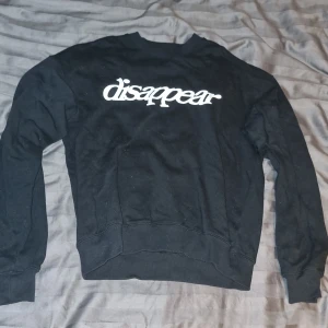 Svart sweatshirt från Vaillent med tryck - Svart sweatshirt från Vaillent i storlek S med vit text 'disappear' tryckt över bröstet. Klassisk rund halsringning och långa ärmar. Tröjan är gjord i mjuk bomull och har en avslappnad passform som passar perfekt till streetwear-stilen.