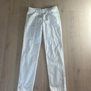 Vita chinos Polo Ralph Lauren - Snygga vita chinos från Polo Ralph Lauren med raka ben och klassisk passform. Byxorna har bälteshällor, knappgylf och två bakfickor med knappar. Tillverkade i mjuk bomull. Storlek 18 år