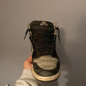 Air Jordan 1 Retro High OG Twist 2.0 Medium Grey - Säljer ett par Nike Air Jordan 1 High i svart och grått skinn. Klassisk siluett med svart swoosh, svarta snören och perforerad tåbox. Högt skaft och retrovibbar, perfekt för dig som gillar streetwear och sneakers med ikonisk design. Pris ej hugget i sten