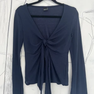 Mörkblå tie front long sleeve top från Gina Tricot - Supersnygg mörkblå top från Gina Tricot med långa ärmar och knyt framtill. Toppens v-ringning och croppade passform ger en trendig look. Perfekt att styla med jeans eller kjol för en cool vibe.