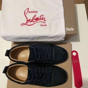 Mörkblå mocka sneakers från Louboutin - Snygga mörkblå sneakers från Christian Louboutin i lyxig mocka med rund tå och platt sula. Skorna har matchande mörkblå snörning och klassisk design som ger en clean och exklusiv vibe. Perfekta för dig som vill sticka ut med stil.