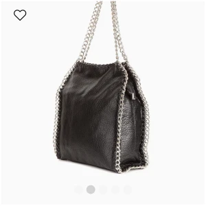 Svart axelväska med kedjedetaljer - Cool svart axelväska i skinn med silverfärgade kedjor längs kanterna och som axelrem. Väskan har en mjuk och fyrkantig form. 
