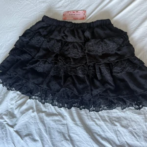 Svart volangkjol med spets från SHEIN - Supersöt svart kortkjol från SHEIN med flera lager volanger och spetsdetaljer. Kjolen har elastisk midja och är perfekt för dig som gillar en lekfull och feminin stil. Materialet känns lätt och flowy, och spetsen ger en extra touch.