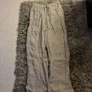Beiga linnebyxor från Zara med snörning - Säljer ett par luftiga och sköna linnebyxor från Zara i beige nyans. Byxorna har elastisk midja med snörning och raka, vida ben. Perfekta för varma dagar och chill vibes. Materialet är linne och ger en avslappnad känsla.